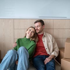 Immobilienkauf: Glückliches Paar sitzt ziwschen Umzugskisten