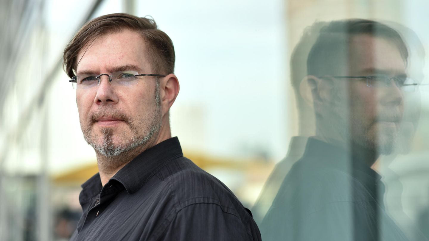 Markus Heitz  lehnt an einer Glasscheibe und spiegelt sich komplett darin.