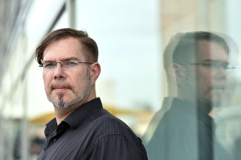 Markus Heitz  lehnt an einer Glasscheibe und spiegelt sich komplett darin.