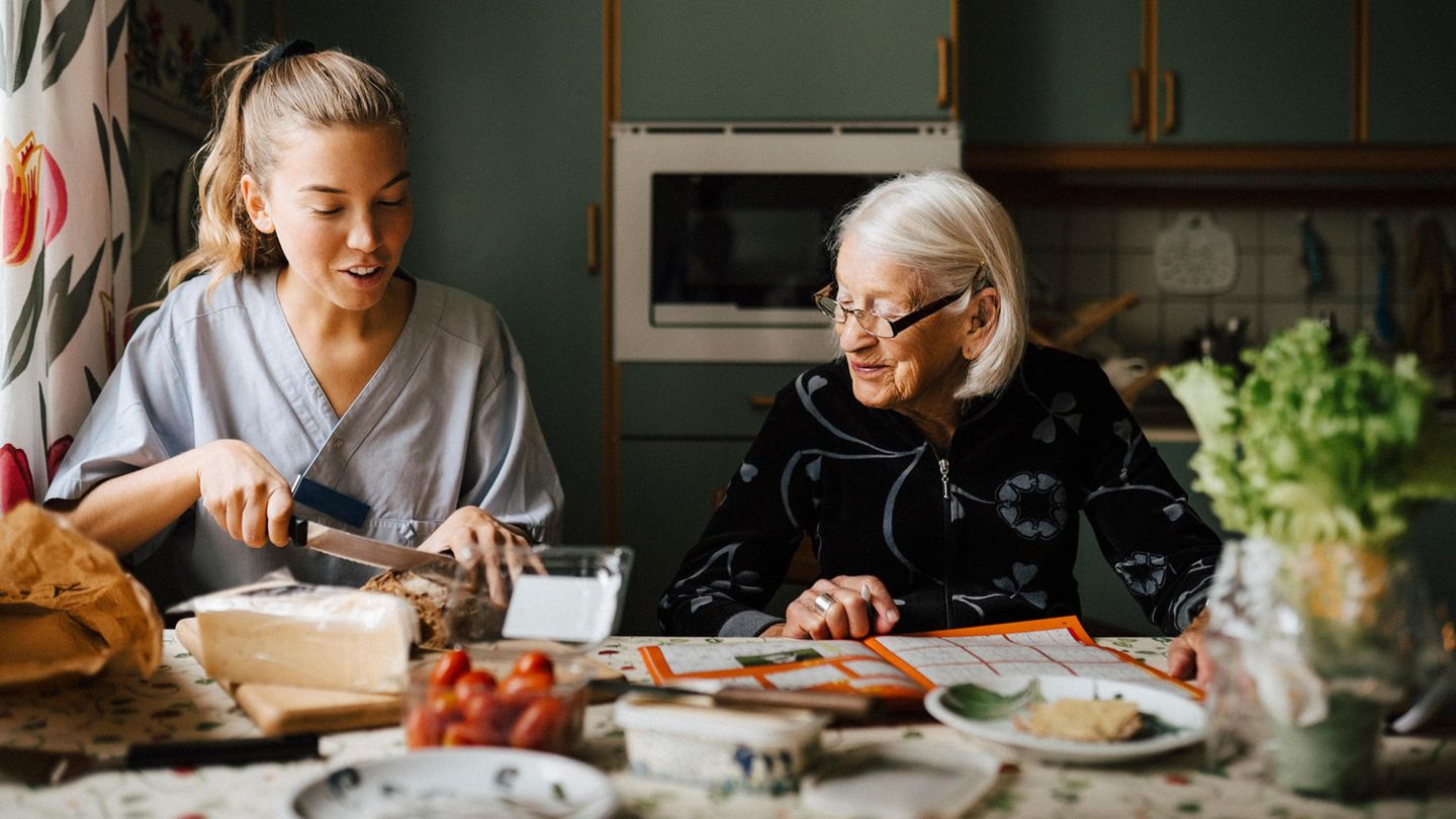 Eine Pflegekraft schneidet Brot für eine alte Dame