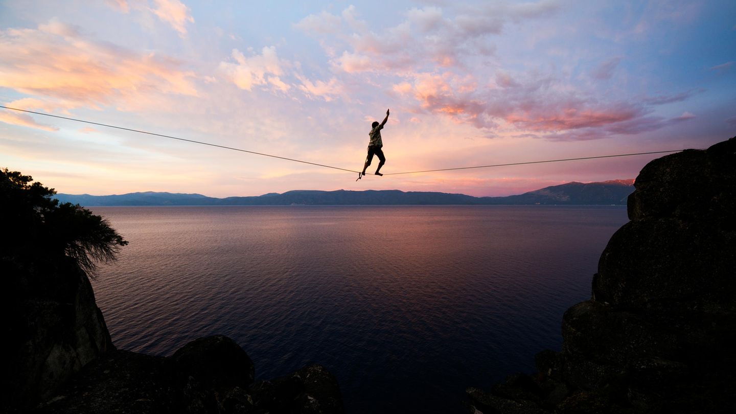 Instabilität (Symbolfoto) Ein Mensch balanciert auf einer Slackline, unter ihm eine Bergschlucht