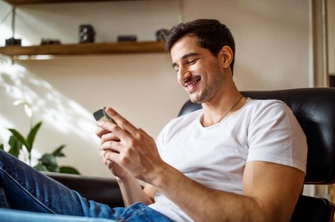 Singles-Day-Deal: Mann sitzt auf dem Sofa mit Handy in der Hand und freut sich.