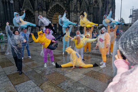 Eine karnevalistische Tanzgruppe aus Belgien posiert bei leichten Nieselregen vor dem Dom für ein Foto