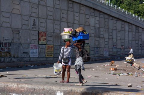 Zwei Frauen laufen mit gepackten Sachen über einen Platz in Port-au-Prince, Haiti