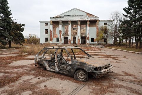 Ein ausgebranntes Autowrack steht vor der Ruine eines neoklassischen Kulturbaus