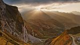 Eine Gipfelkette mit Strahlen der Abendsonne und den Serpentinen des Alpenpasses Colle di Tenda