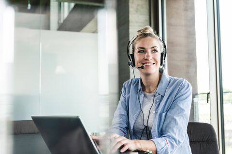 Frau mit Headset vor dem Computer freut sich über den Black Week Business-Deal.