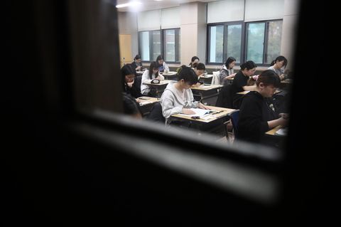 durch ein Fenster sieht man Schüler in einem Klassenraum bei einer Prüfung in Südkorea