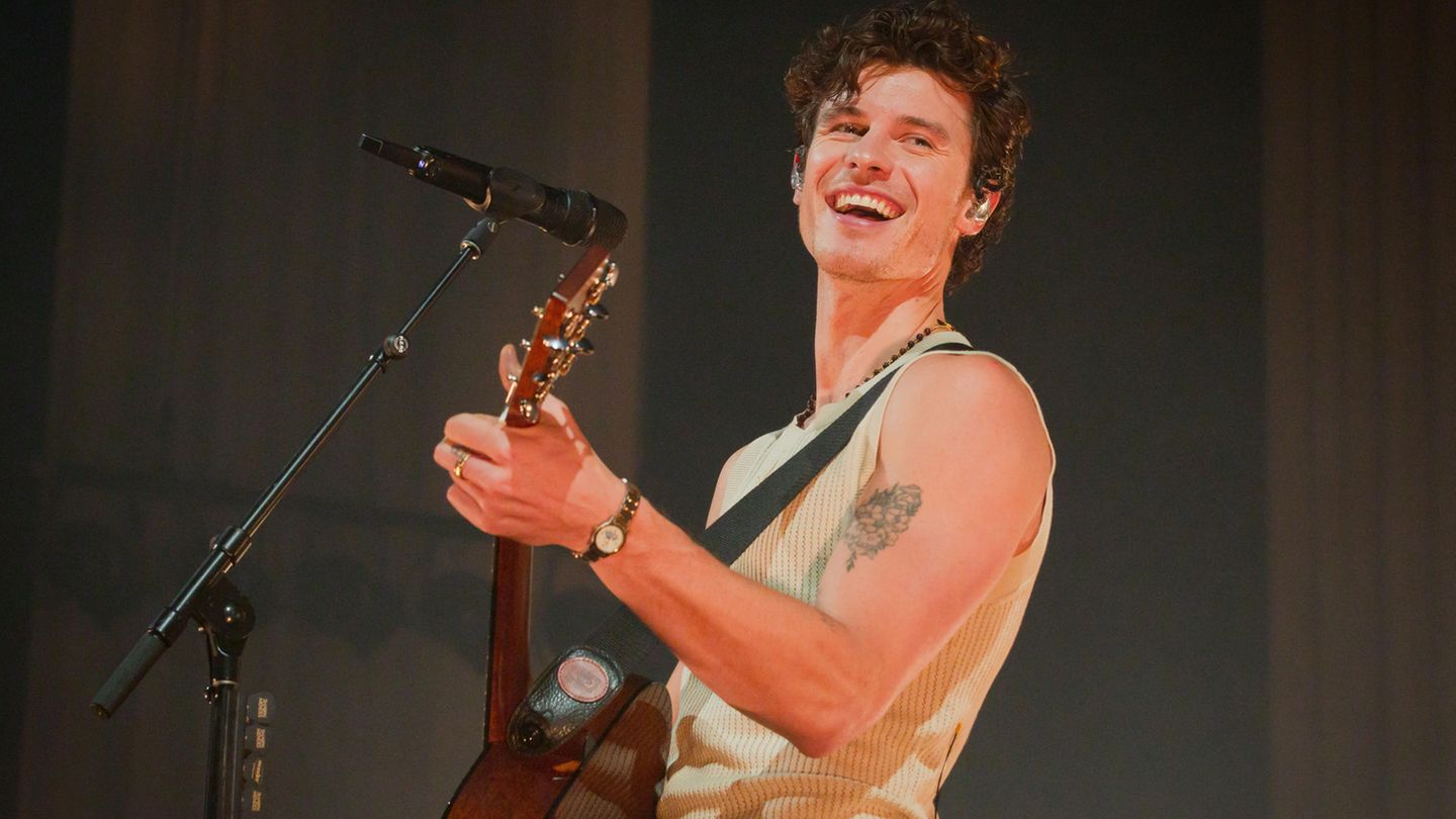 Shawn Mendes lacht in Berlin in die Kamera, während er im Unterhemd Gitarre spielt