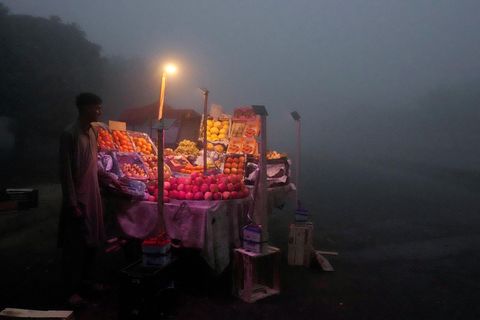 Ein Obsthändler steht im Licht einer Lampe auf der Straße neben seinem Obststand