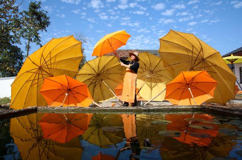 Eine Arbeiterin hat sieben orangene Schirme aufgespannt und steht vor einem Becken in dem sich die Schirme spiegeln