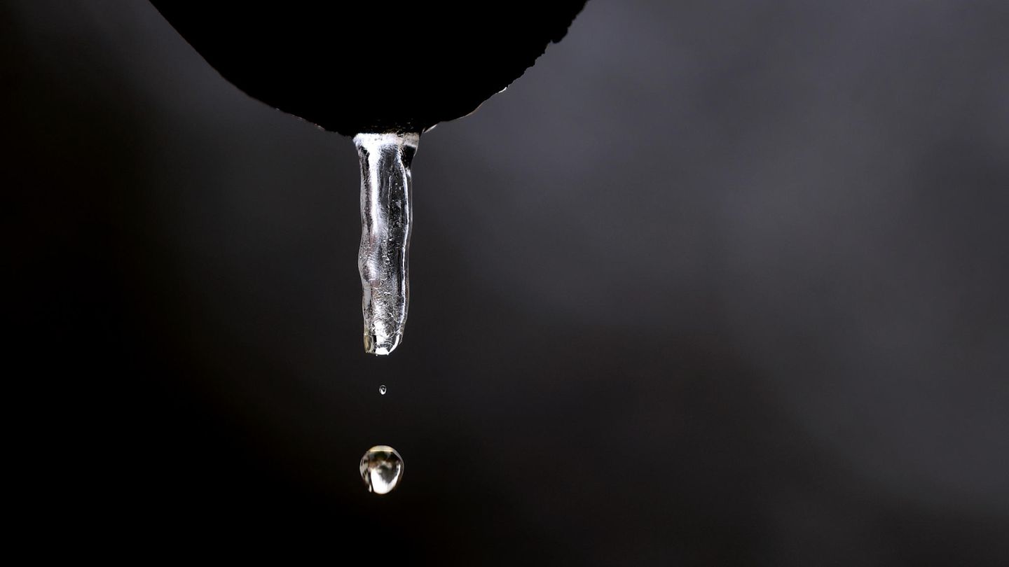 Wasser tropft aus einem tauenden Eiszapfen, der an einer Dachrinne hängt