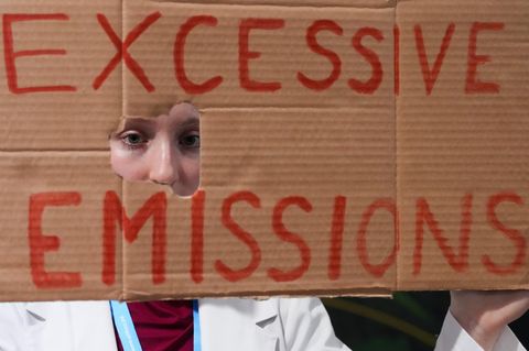 Eine Aktivistin hält ein Plakat mit den Worten "Excessive Emissions" vor ihr Gesicht