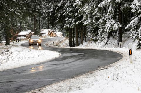 Ein Auto fährt auf einer nassen Straße durch einen Wald voller Schnee