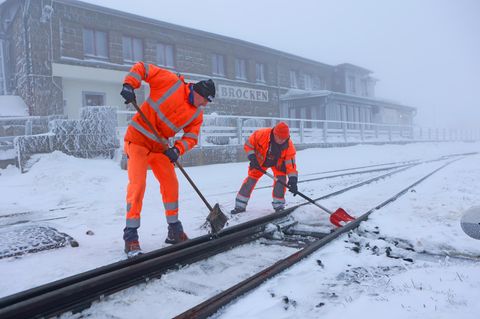 Mitarbeiter der Harzer Schmalspurbahnen GmbH schaufeln Schnee aus den Weichen des Brockenbahnhofes.