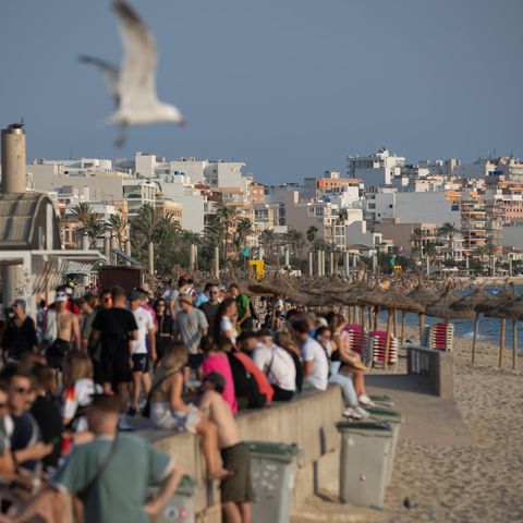 Urlauber spazieren am Strand von El Arenal auf Mallorca, Spanien, viele sitzen auf der Mauer am Strand
