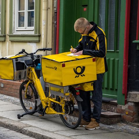 Ein Postbote unterschreibt einen Zettel auf einem Fahrrad