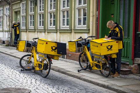 Ein Post-Zusteller unterschreibt auf einem Fahrrad ein Stück Papier