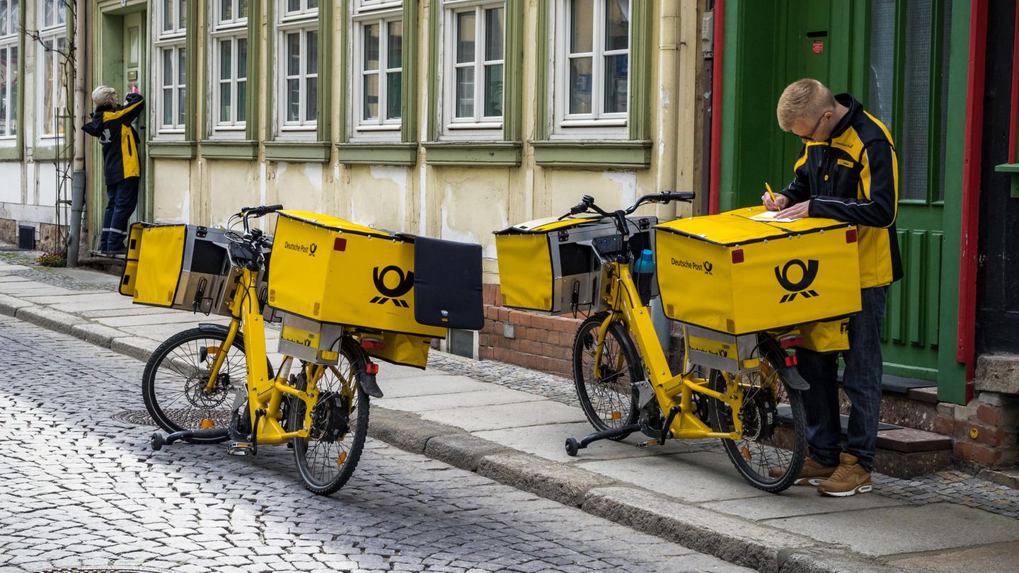 Ein Post-Zusteller unterschreibt auf einem Fahrrad ein Stück Papier