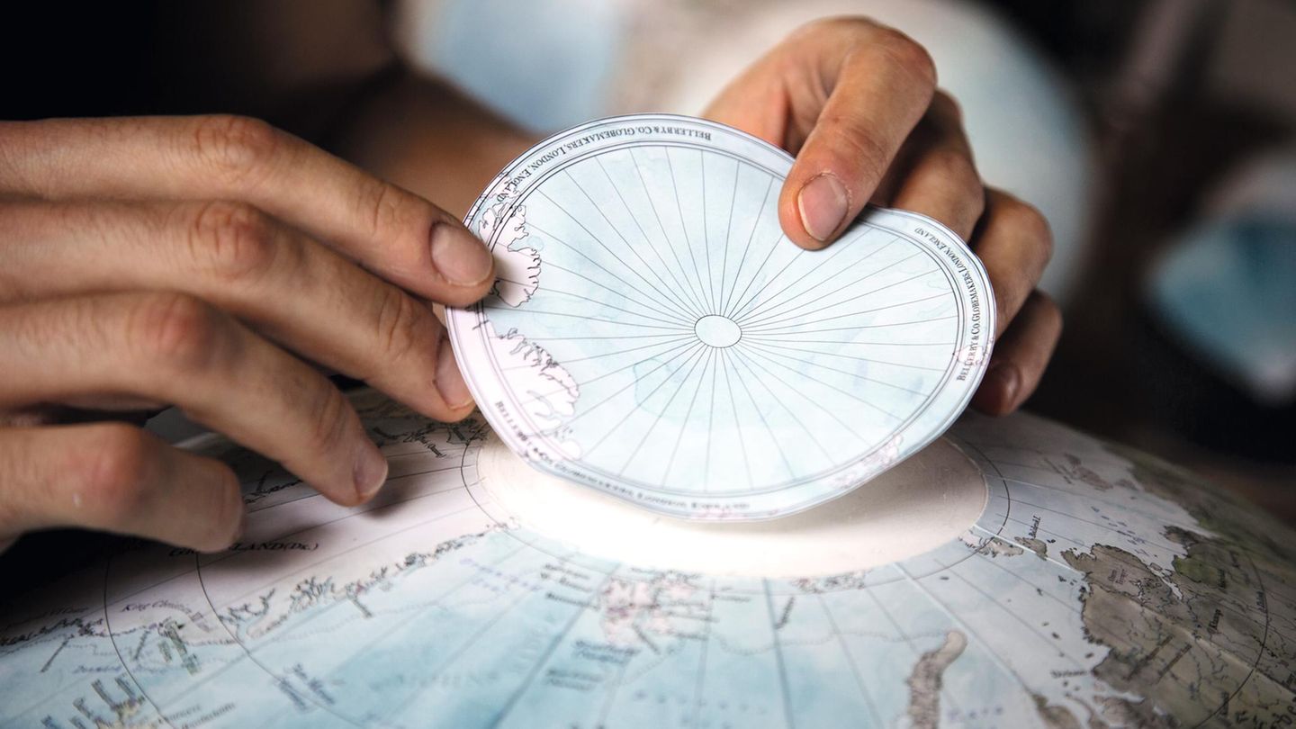 Zwei Hände kleben die Papierscheibe mit dem Nordpol oben auf einen Globus