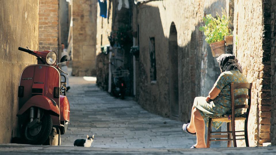 Eine alte Frau sitzt in der Straße eines italienischen Dorfes