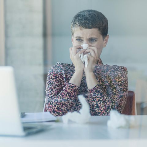 Frau putzt sich vor Laptop die Nase. Wegen eines Schnupfens bekommt niemand die Kündigung
