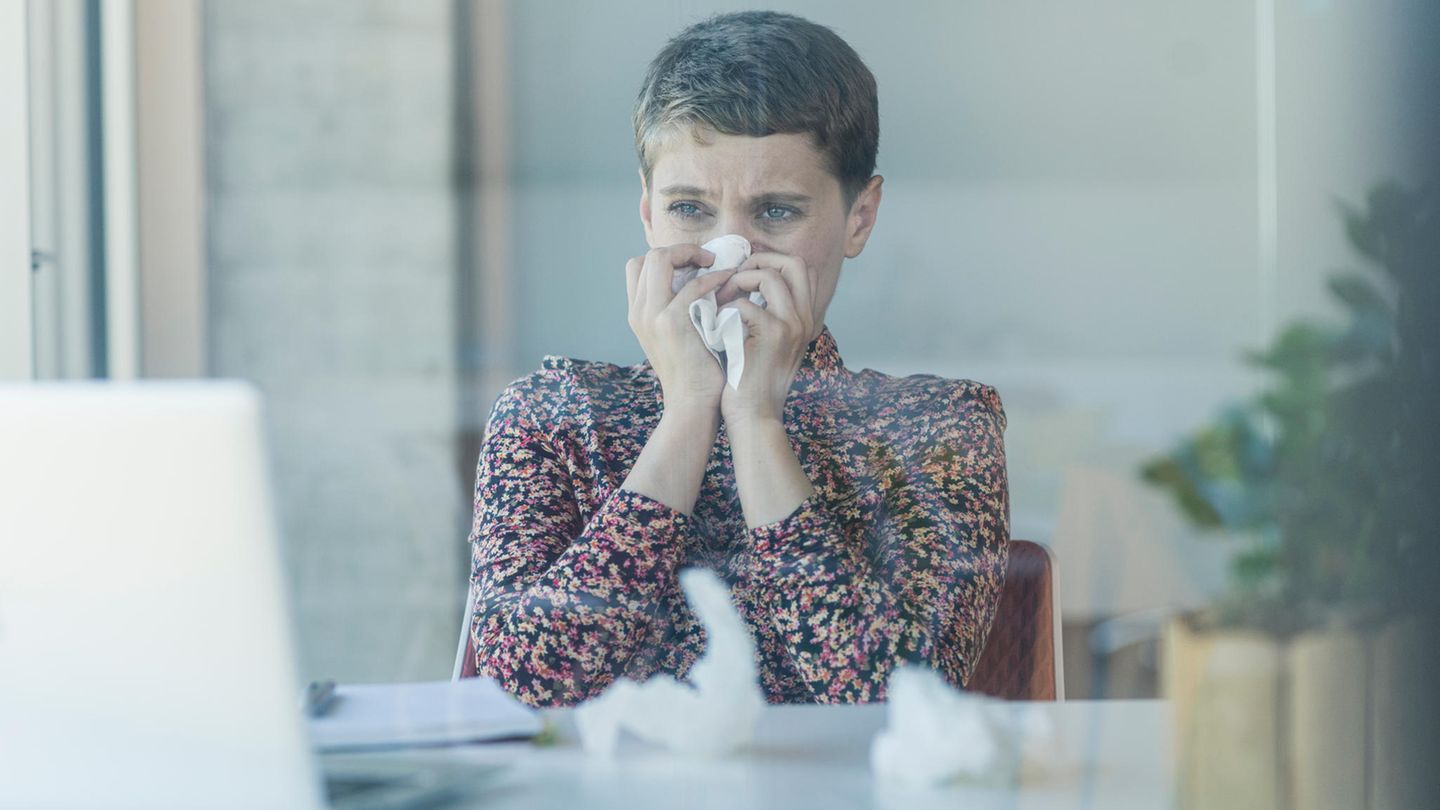 Frau putzt sich vor Laptop die Nase. Wegen eines Schnupfens bekommt niemand die Kündigung