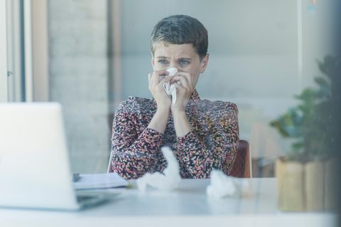 Frau putzt sich vor Laptop die Nase. Wegen eines Schnupfens bekommt niemand die Kündigung