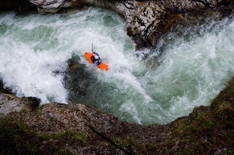 Kajakfahrer fährt im orangenen Kajak zwischen Felsen einen Fluss hinunter