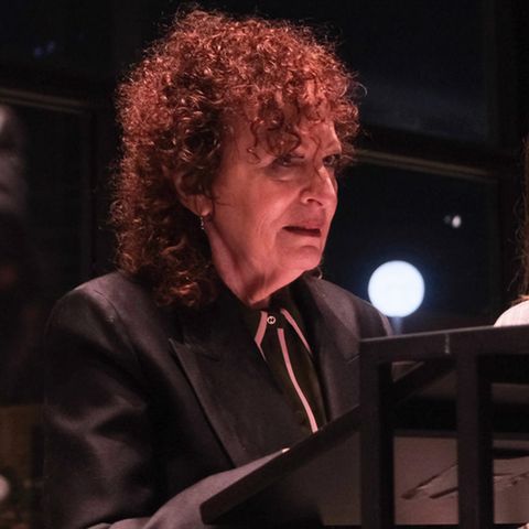 Nan Goldin stands at the lectern in the Neue Nationalgalerie in Berlin, several people hold up cell phones and film her