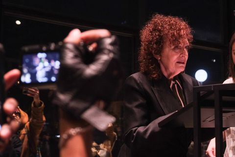 Nan Goldin steht am Redepult in der Neuen Nationalgalerie in Berlin, mehrere Leute halten Handys hoch und filmen sie