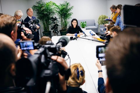 Annalena Baerbock sitzt am Ende eines Tisches in einem Konferenzraum des Klimagipfels, umringt von Kameraleuten und Reportern