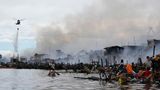 Ein Hubschrauber nährt sich mit Wasser zum Löschen, im Wasser vor dem Brand sind Bewohner mit ihren Sachen zu sehen