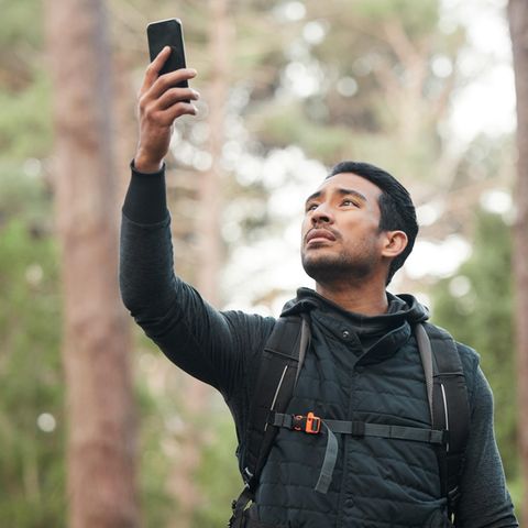 Ein Mann sucht im Wald nach Empfang im Handynetz
