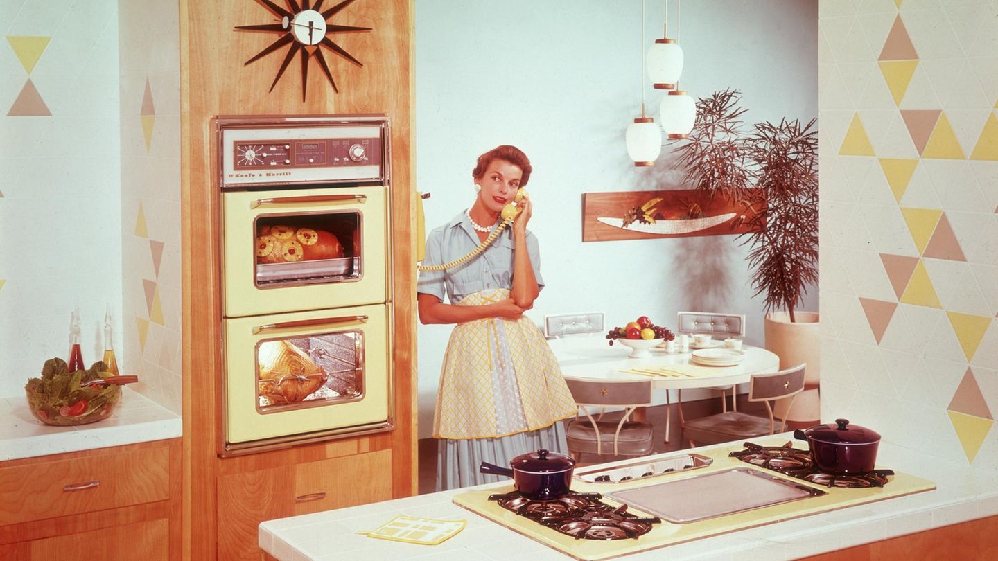 Tradwife: Eine Hausfrau aus den 50ern, steht in ihrer Küche, das Essen im Ofen und telefoniert