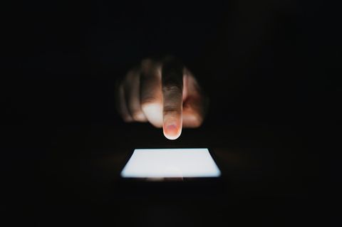 Eine Hand im dunklen über einem Handybildschirm der leuchtet