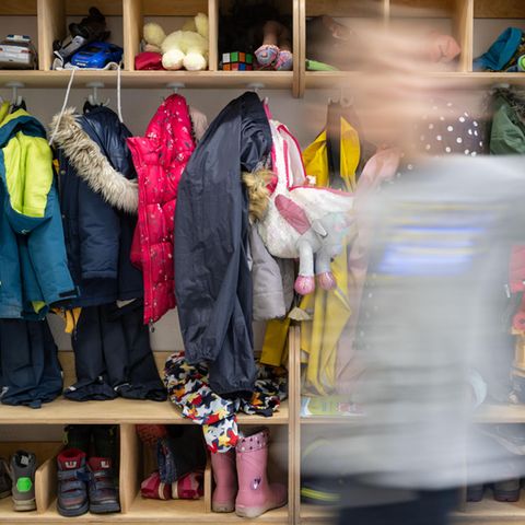 Ein Kind einer Kindergartengruppe läuft an der vollen Garderobe vorbei