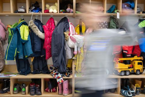 Ein Kind einer Kindergartengruppe läuft an der vollen Garderobe vorbei