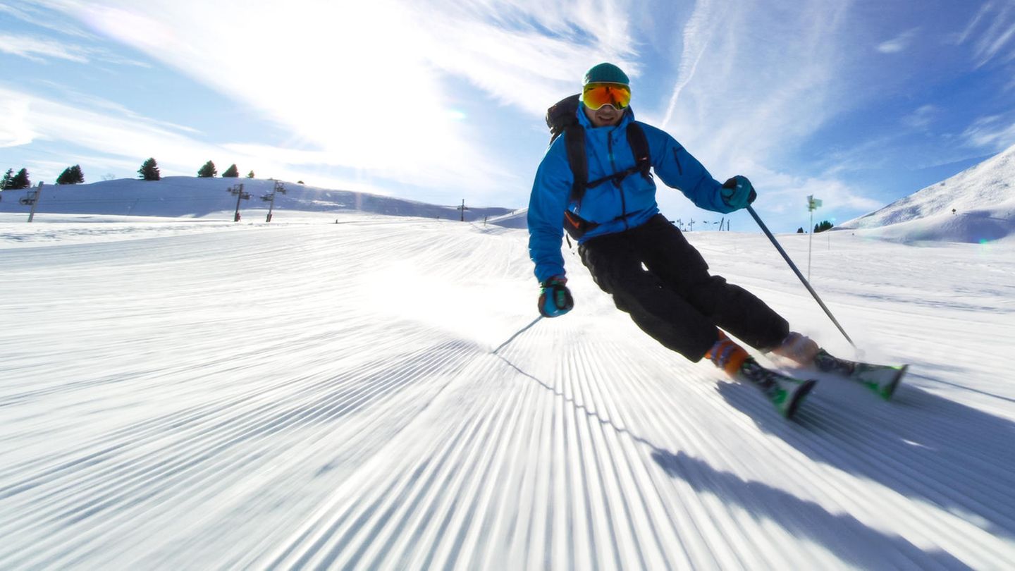 Ein Mann in Skiausrüstung fährt unter leicht bewölktem Himmel eine Piste im Skiurlaub