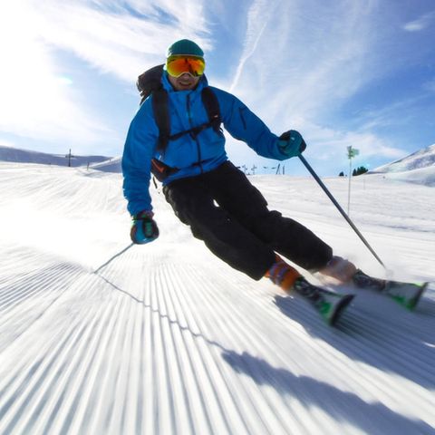 Ein Mann in Skiausrüstung fährt unter leicht bewölktem Himmel eine Piste im Skiurlaub