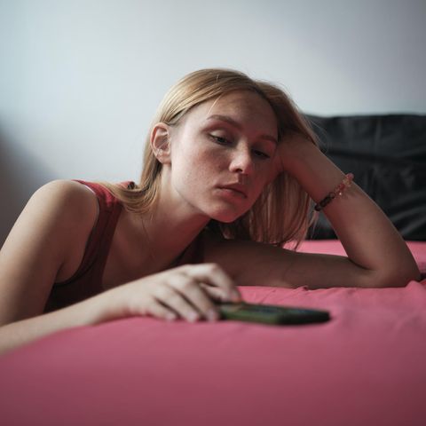 Dating-Krise: Frau lehnt am Bett, Handy in der Hand