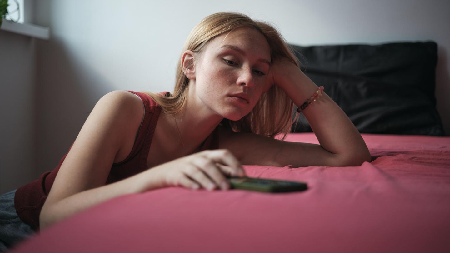 Dating-Krise: Frau lehnt am Bett, Handy in der Hand