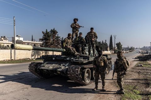 Syrische Oppositionskämpfer stehen auf und neben einem erbeuteten Panzer des syrischen Regimes in der Provinz Aleppo