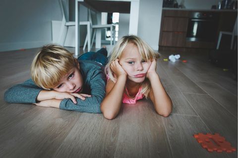 Zwei Kinder liegen gelangweilt auf dem Wohnzimmerboden