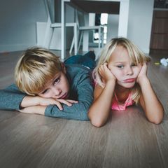 Zwei Kinder liegen gelangweilt auf dem Wohnzimmerboden