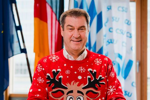 Markus Söder sitzt in einem Weihnachtspullover vor einem Advenskranz