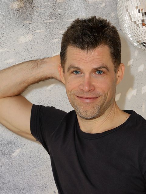 Bas Kast lehnt mit einem Arm an der Wand und lächelt.