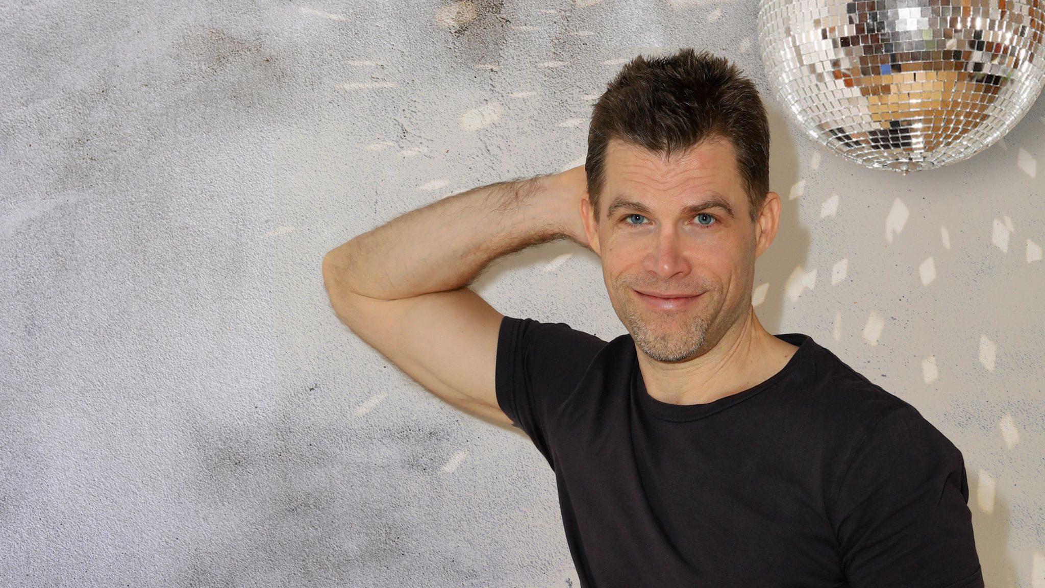 Bas Kast lehnt mit einem Arm an der Wand und lächelt