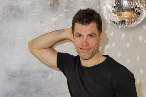 Bas Kast lehnt mit einem Arm an der Wand und lächelt