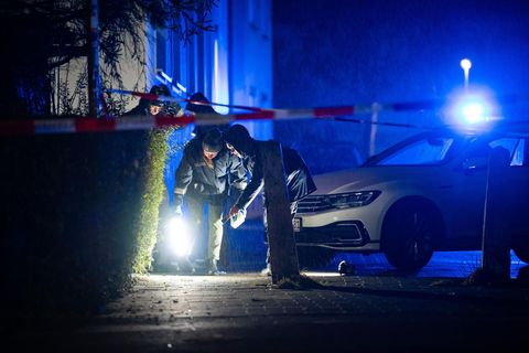 Neben einem Auto mit Blaulicht suchen zwei Polizisten mit Taschenlampen den Boden in Kiel ab